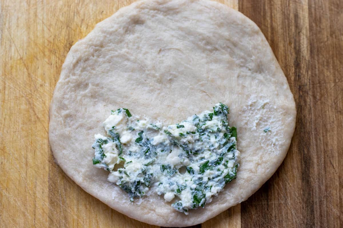 a spoonful of cheese filling is placed on the side of the dough to form a half moon shaped pogaca