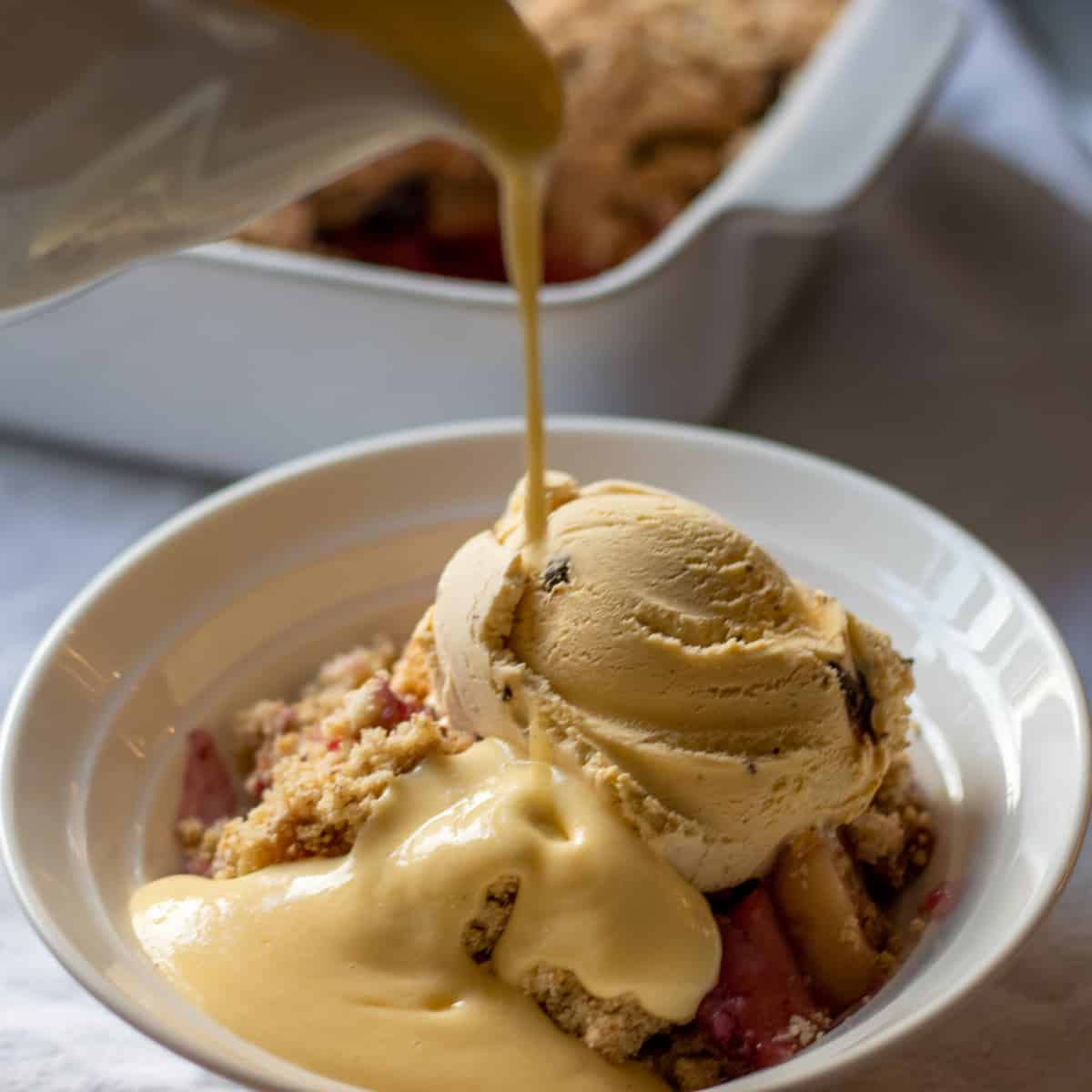 pouring custard over a bowl of apple crisp without oats