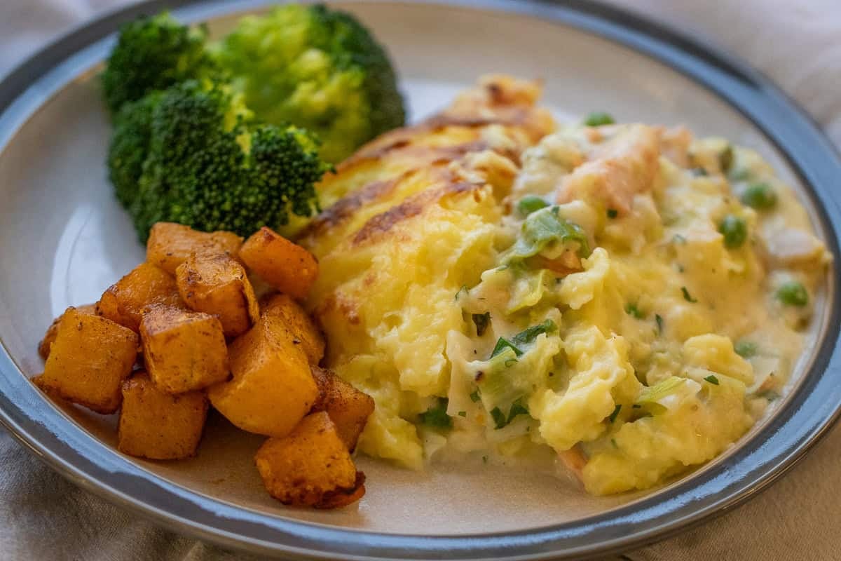 a plate of fish pie served with butternut squash and green veggies