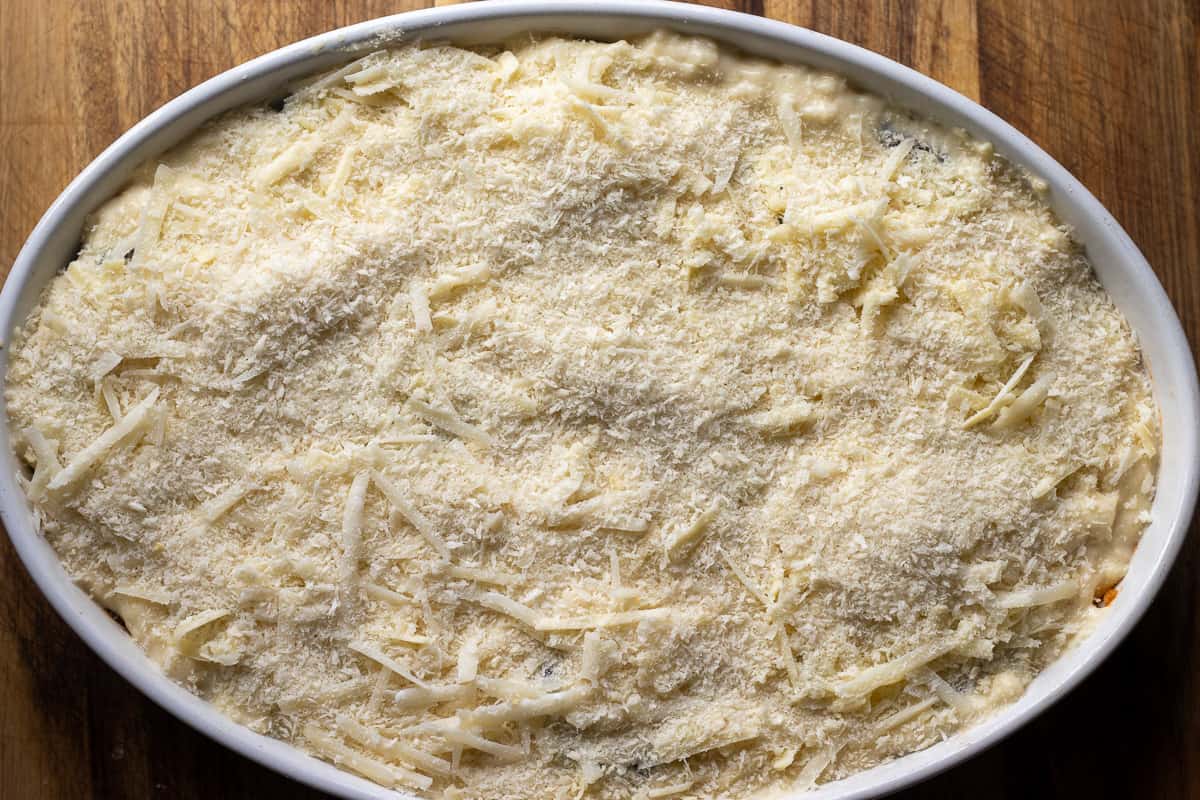 the moussaka dish is topped with cheese and breadcrumbs before baking