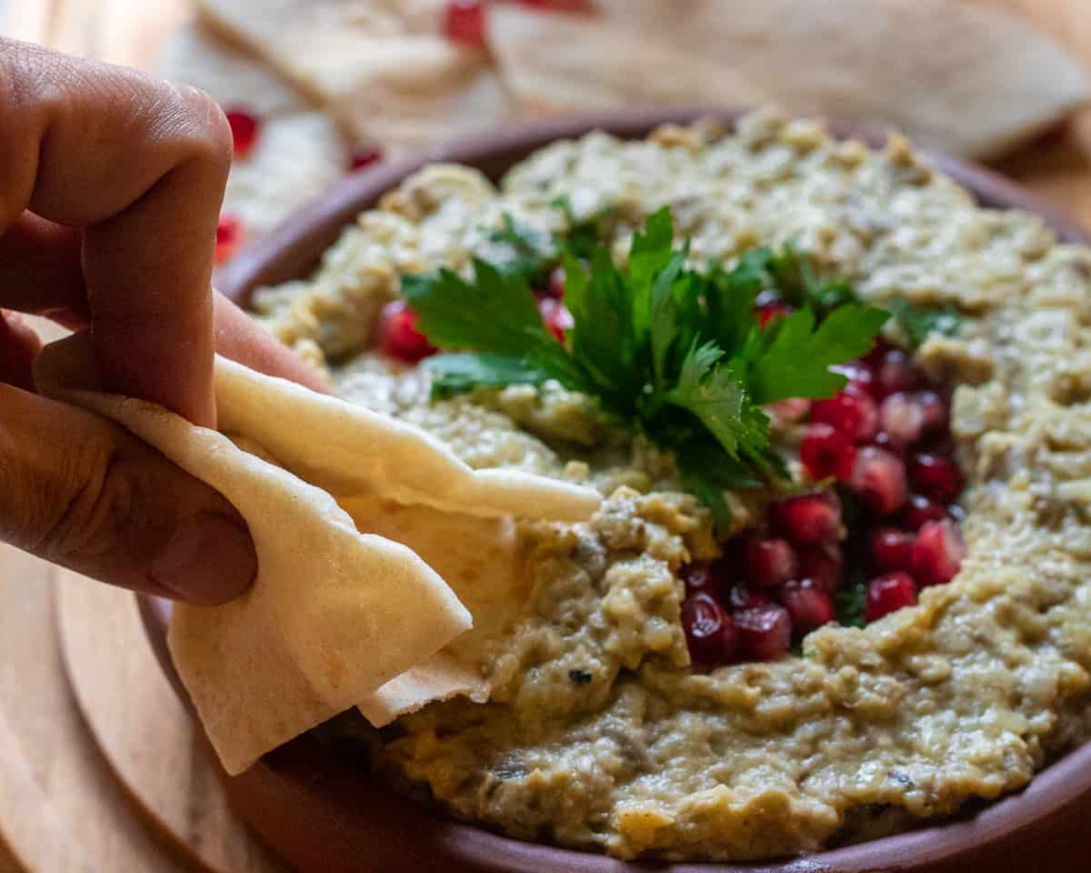 dipping a piece of pita bread in baba Ganoush