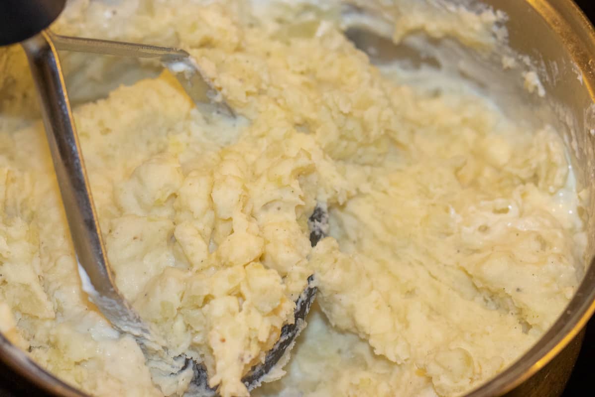 mashing the cooked potatoes using a masher