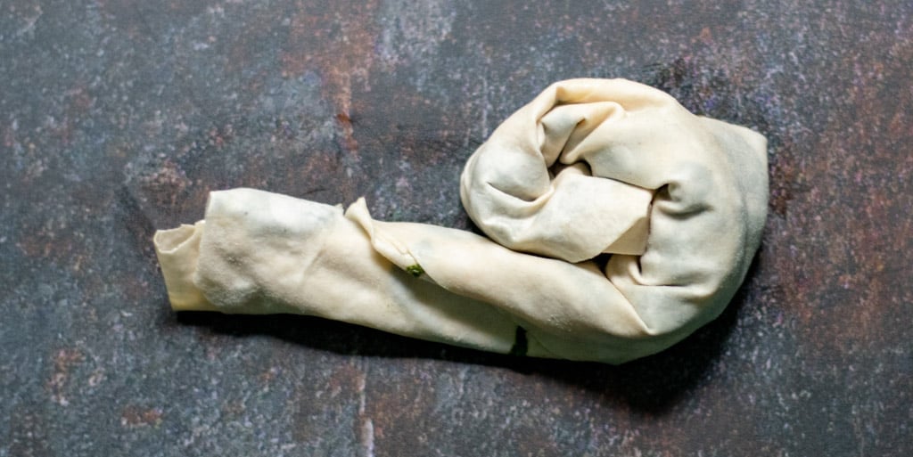 Take one of the triangles and roll it starting from the large side into a long sausage shape.