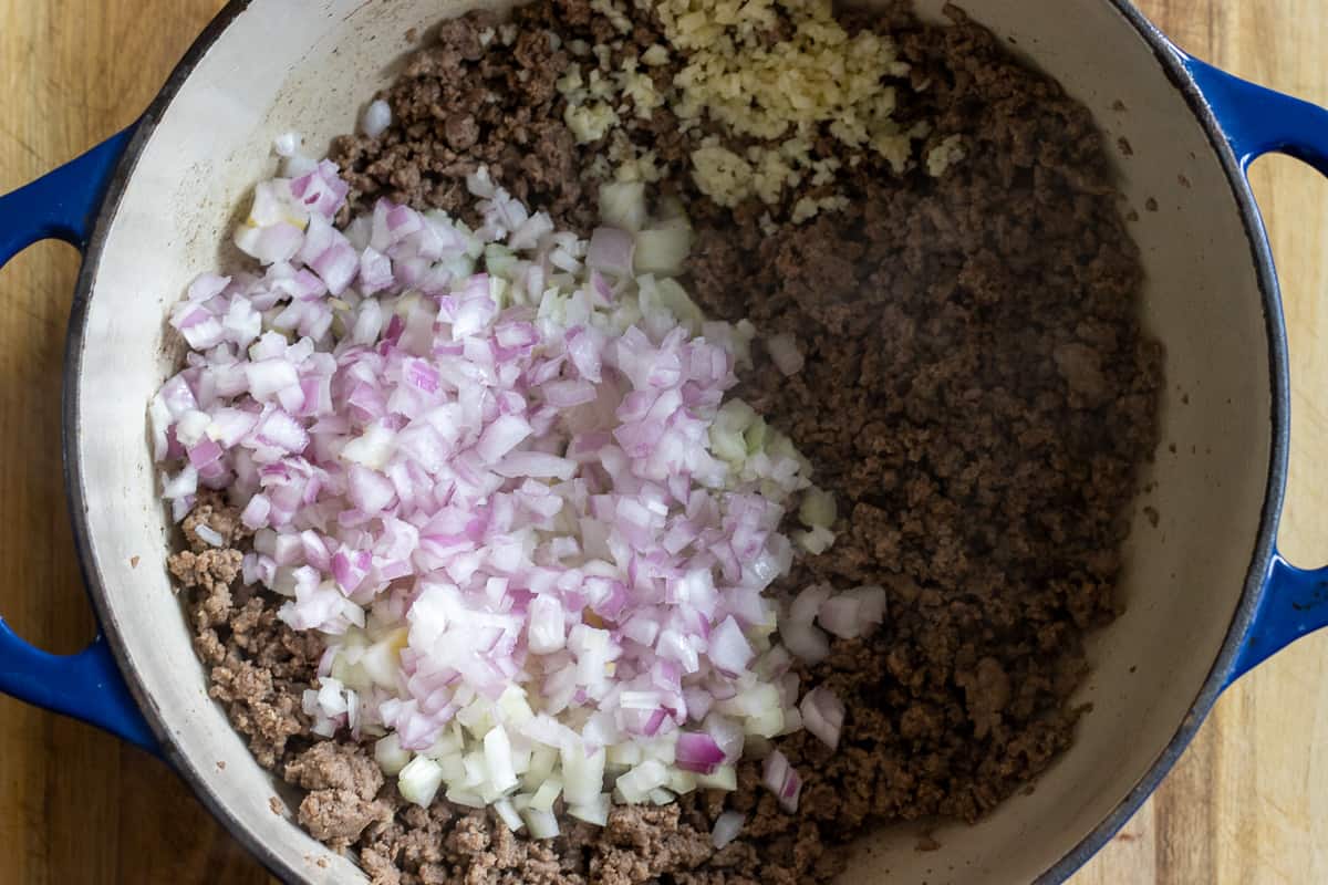 Sautéing the onions and garlic in a Dutch oven along with the ground beef.