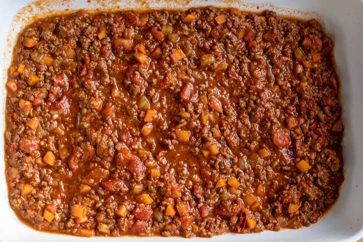 Meat sauce is spread to the bottom of an oven dish.