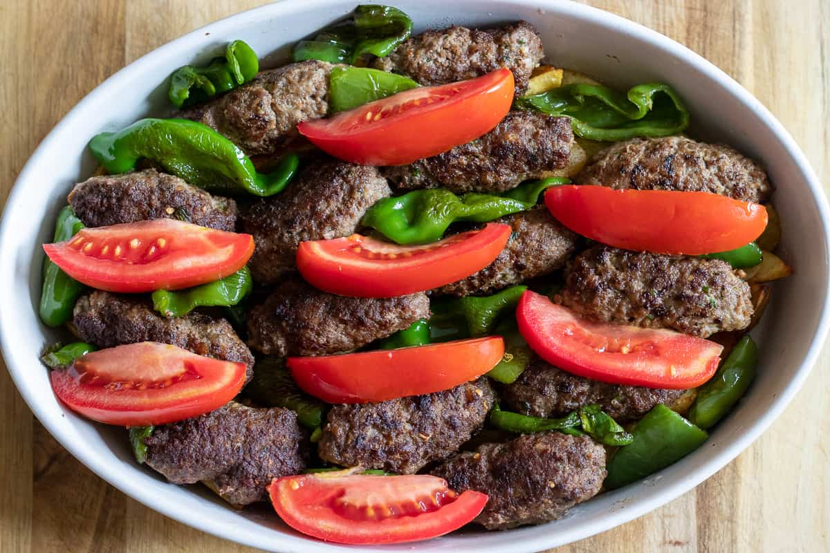 meatballs, peppers and tomato wedges are scattered on top of potatoes