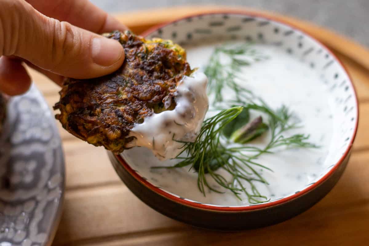 a piece of Mucver (Turkish Zucchini Fritters) is dipped in yogurt