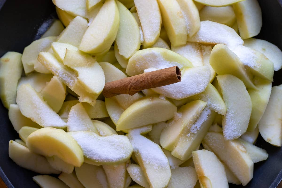 sliced apples are placed in a pan with a cinnamon stick and sugar