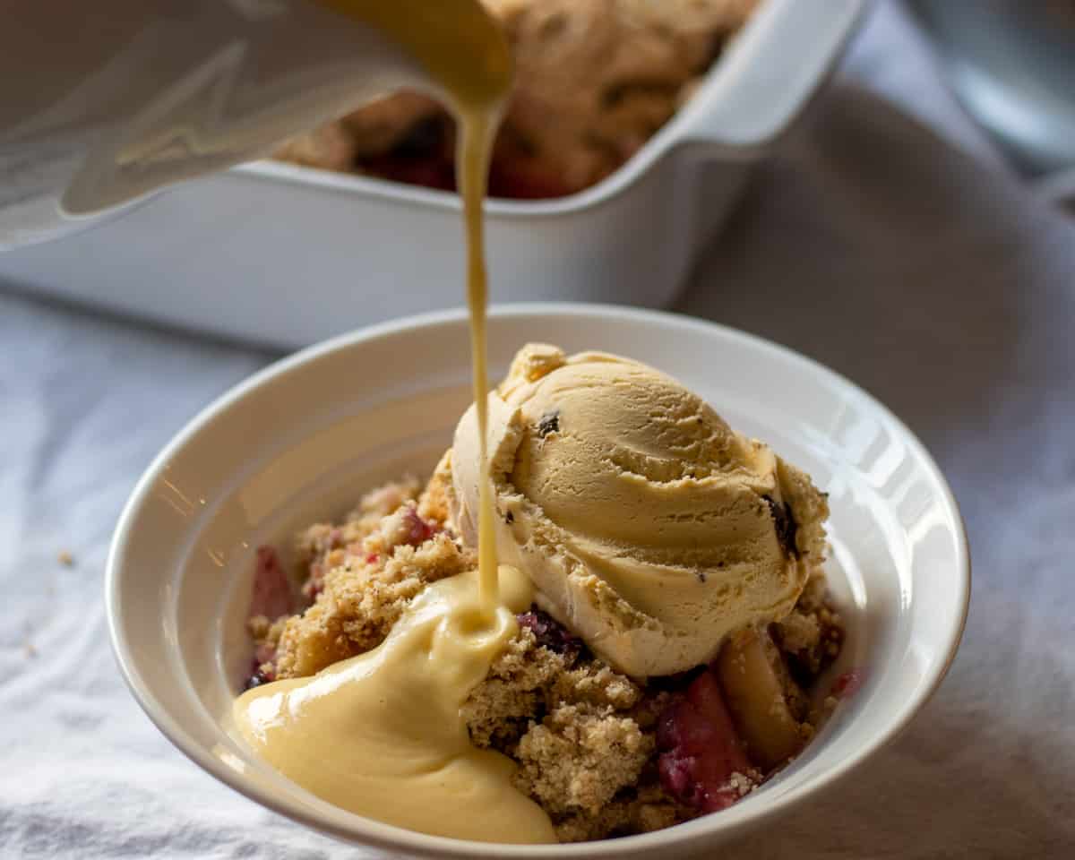 pouring homemade custard over apple and blueberry crumble
