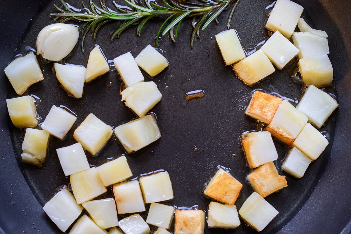 parboiled potatoes are in a pan with rosemary, garlic and oil
