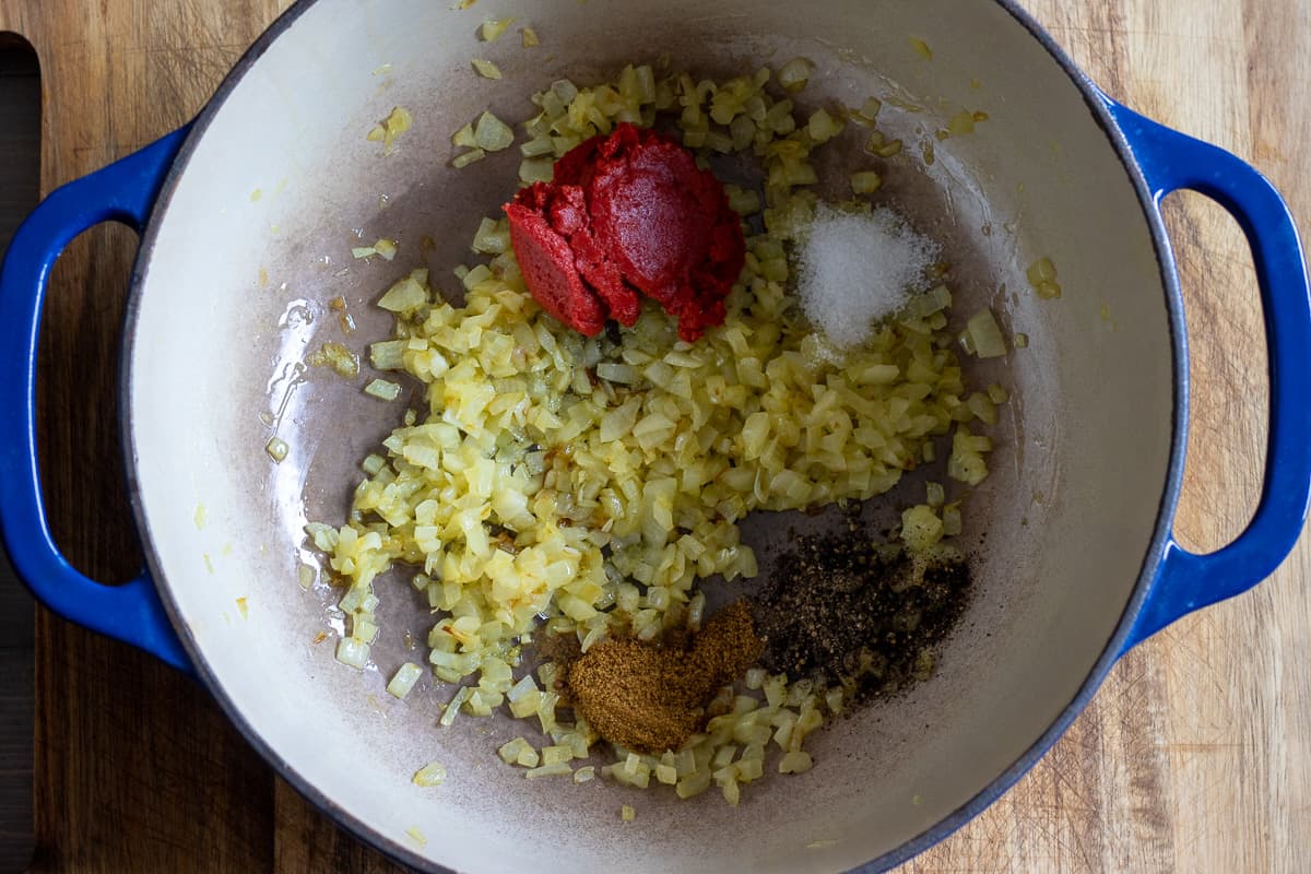 garlic, tomato paste, salt, pepper, and cumin are added to sautéed onions for making vegan Lebanese eggplant moussaka - maghmour dish