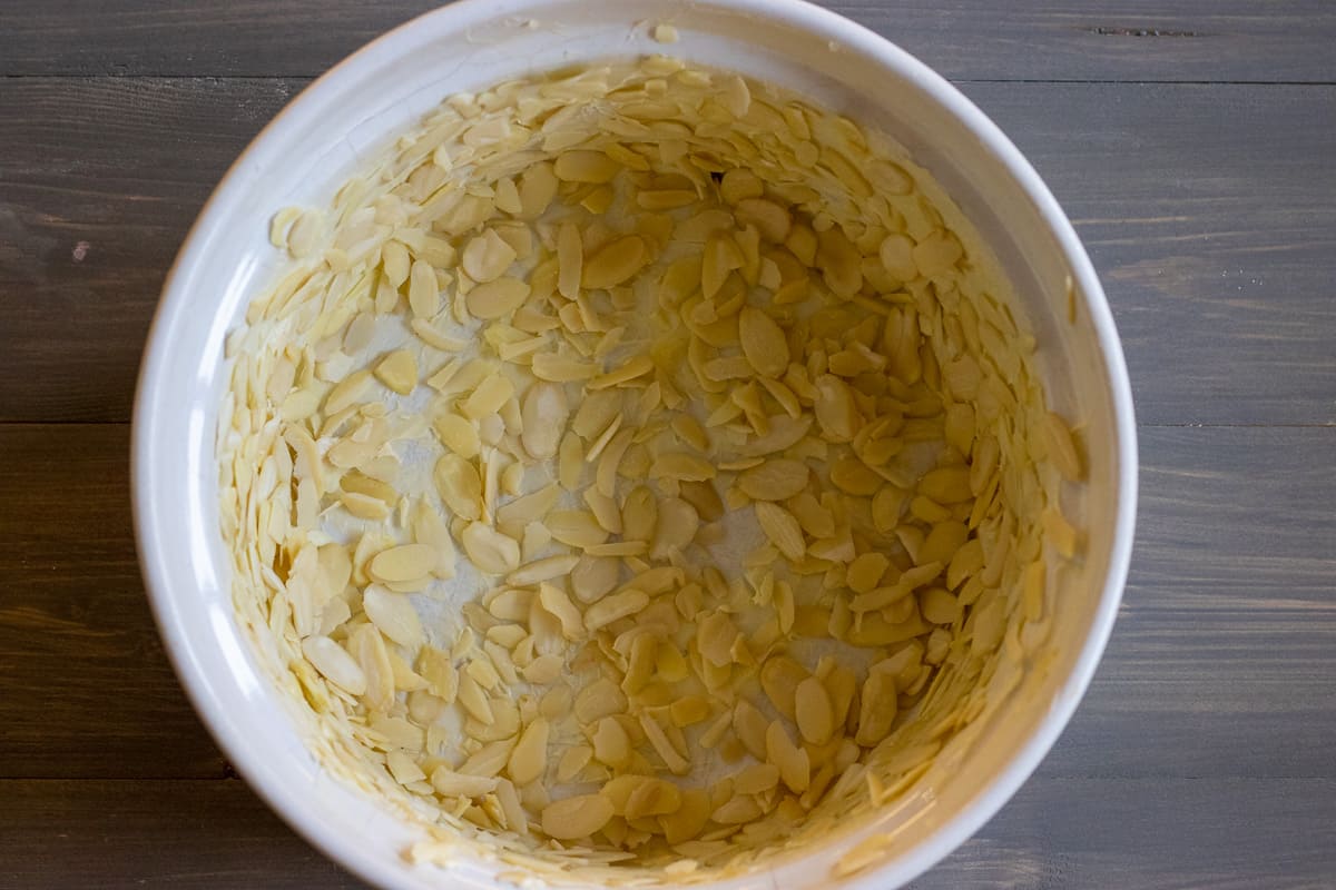 the sides and the bottom of an oven dish is buttered and covered with almonds