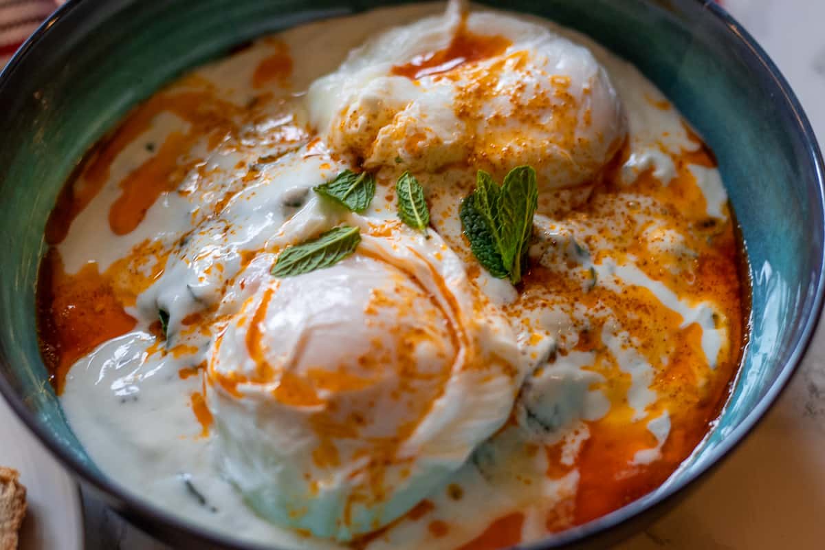 A bowl of poached eggs with yogurt sauce and bread