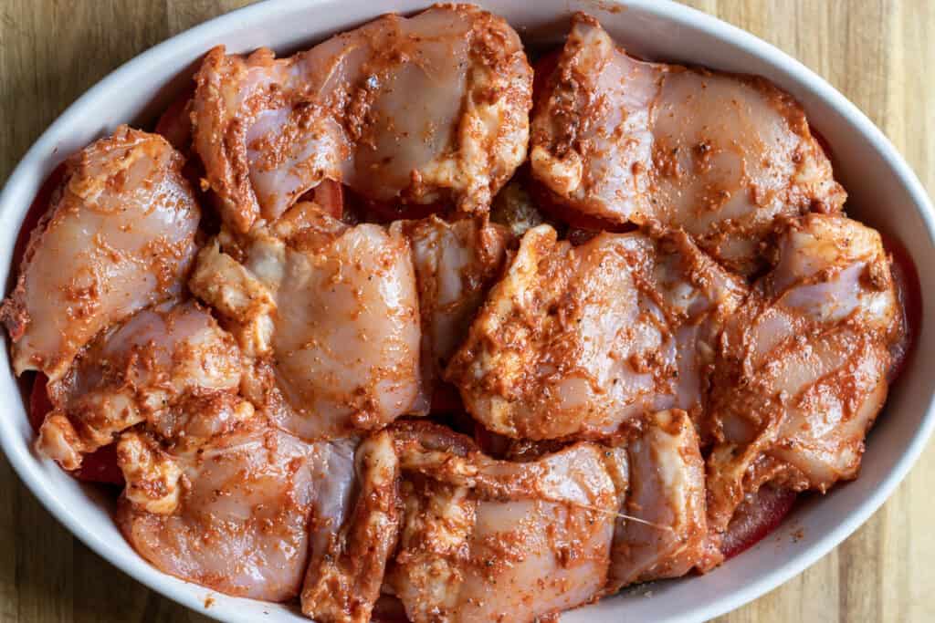 Marinated chicken pieces are scattered on top of the vegetables.