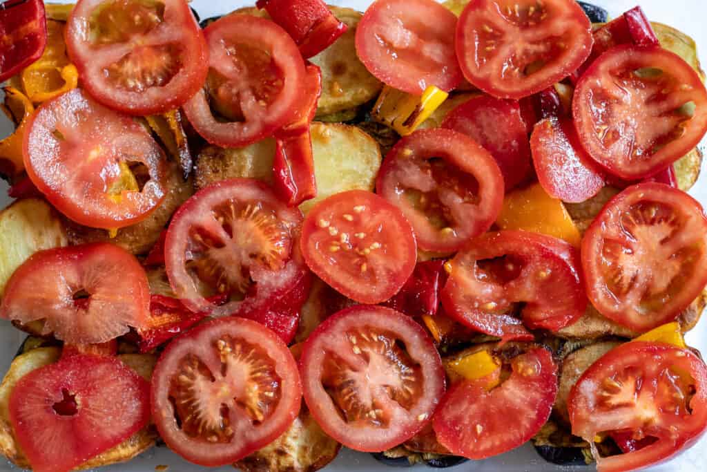 Sliced tomatoes and peppers are arranged on top of the potatoes.