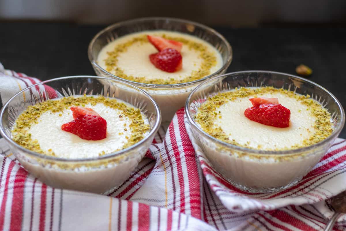 3 bowls of keskul served with ground pistachio and strawberries