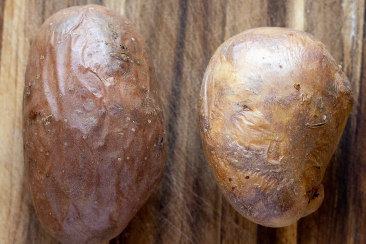 2 baked potatoes on a cutting board