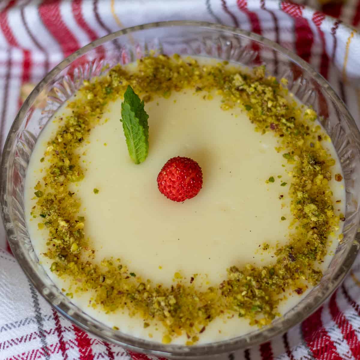 muhalabiah served in a glass bowl and garnished with a wild strawberry, mint leaves and ground pistachio