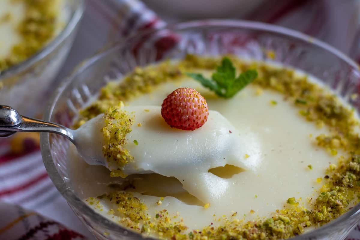 a spoonful of muhallebi dessert garnished with wild strawberry and pistachio 