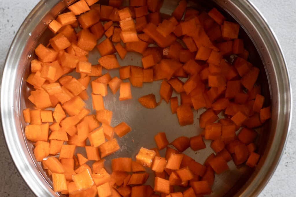 Diced carrots are in a pan filled with cold water.