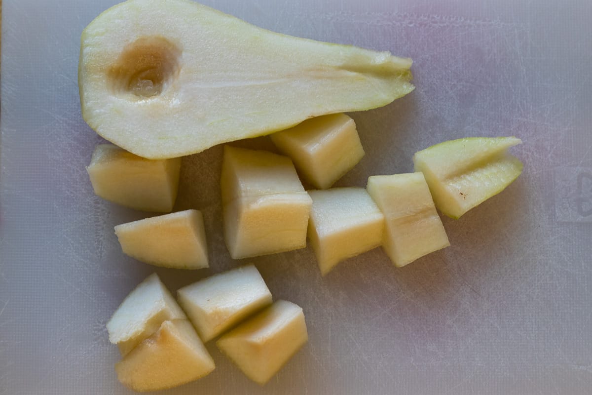 A pear is cut in half, peeled, cored, and cut into cubes.
