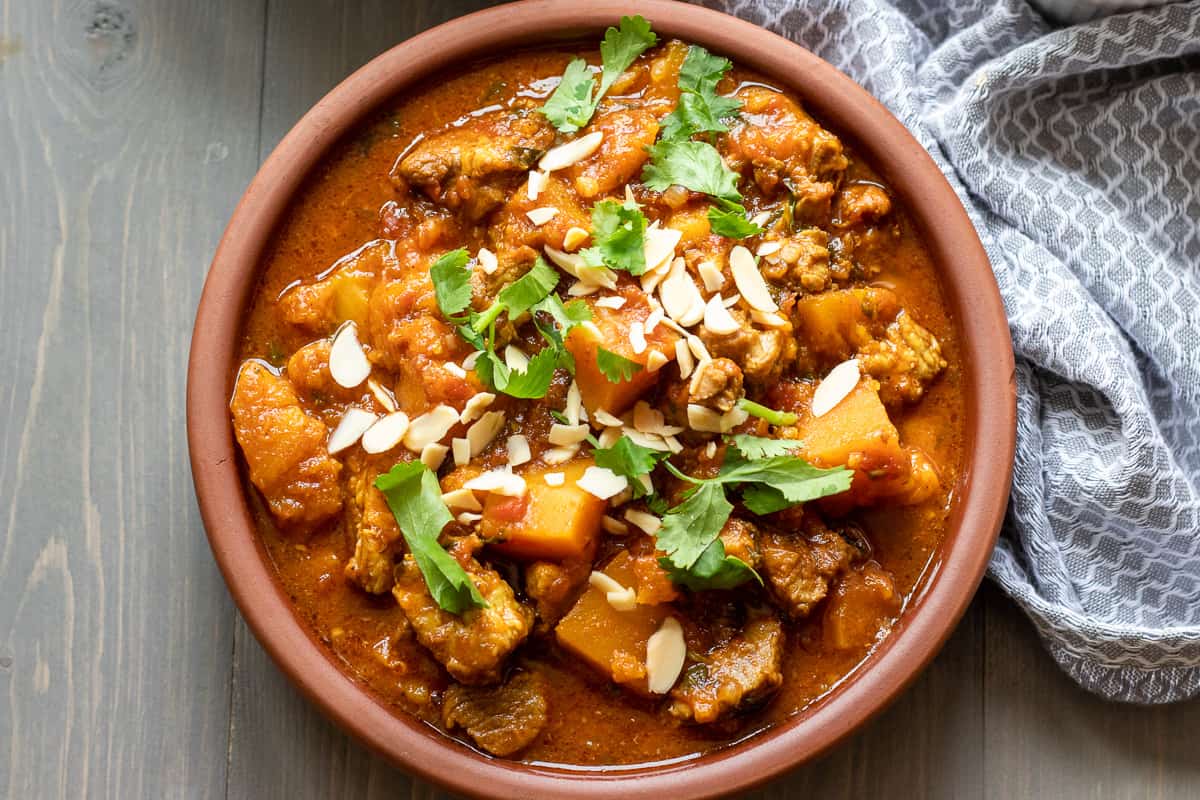 slow cooked lamb tagine with apricots and squash is served with coriander leaves and flaked almonds