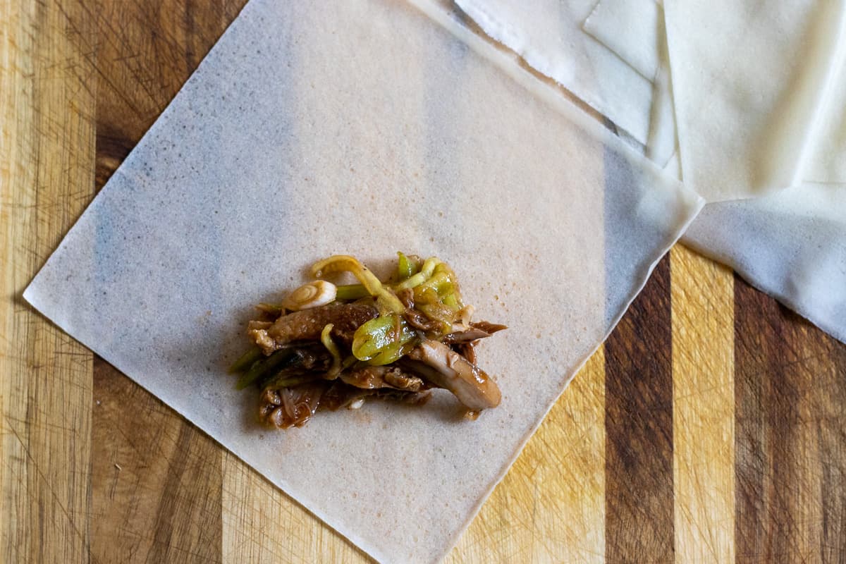 a piece of wrapper is placed on a cutting board and topped with duck filling