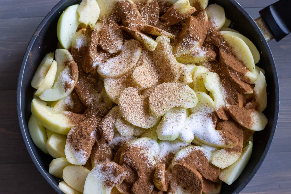 sliced apples are placed in a pan with cinnamon, nutmeg and sugar