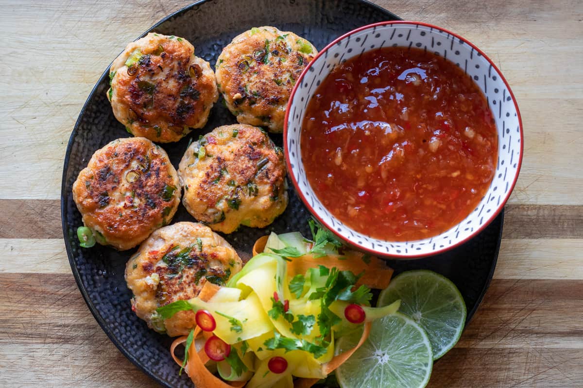 thai fish cakes are fried and served with a bowl of chili sauce and salad