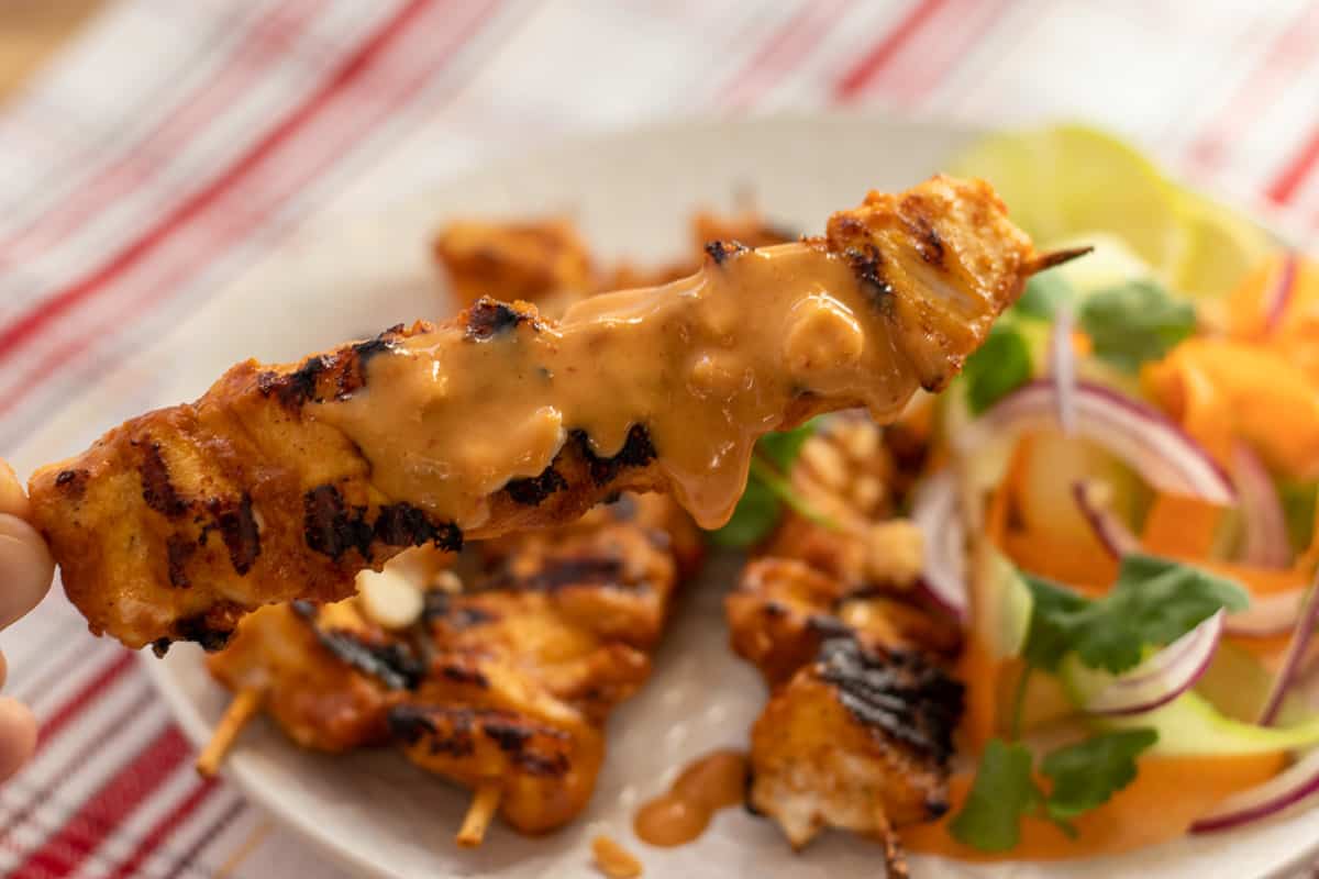A piece if Thai chicken skewer is dipped in peanut sauce.