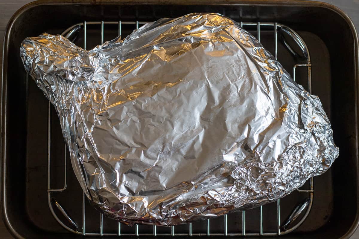 lamb shoulder wrapped in tin foil is placed on a rack