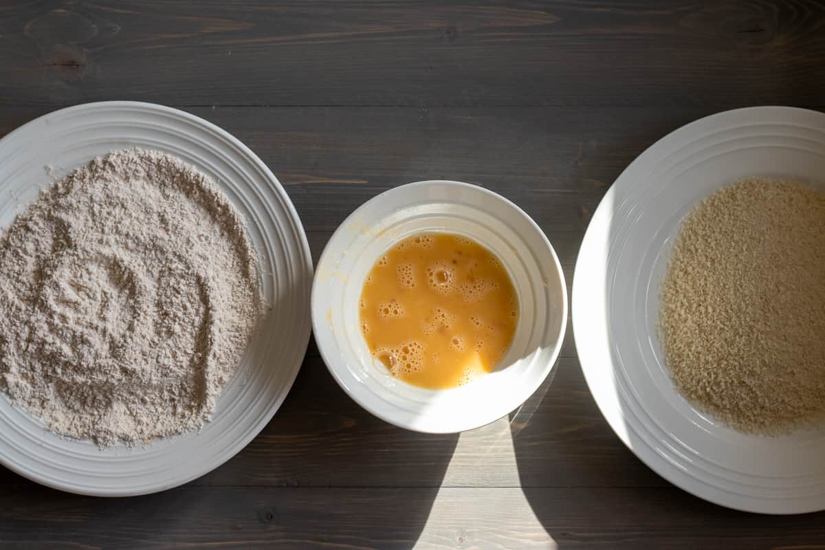 flour, eggs and breadcrumbs are placed in plates for breading the chicken tenders