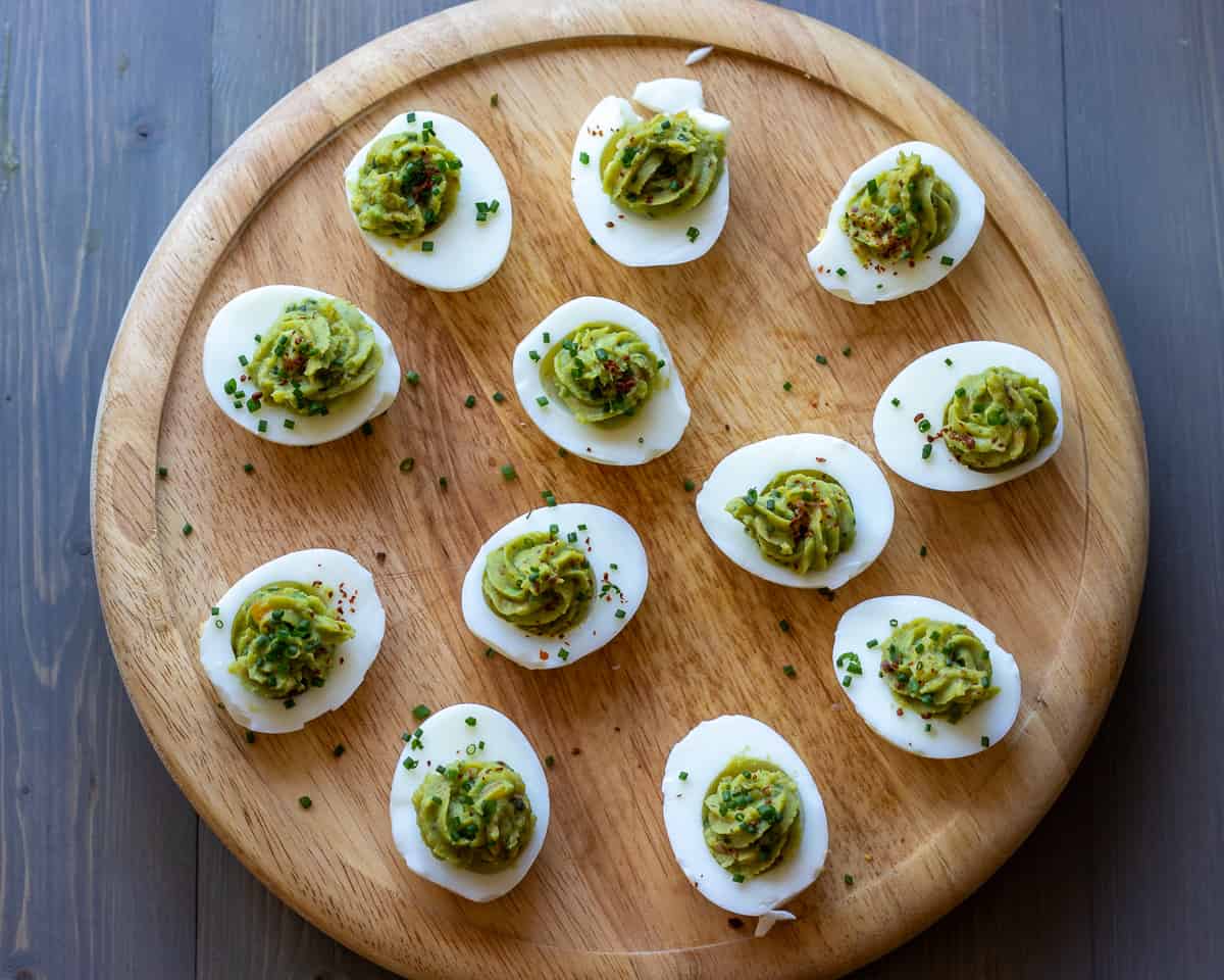 12 pieces of avocado devilled eggs on a wooden plate