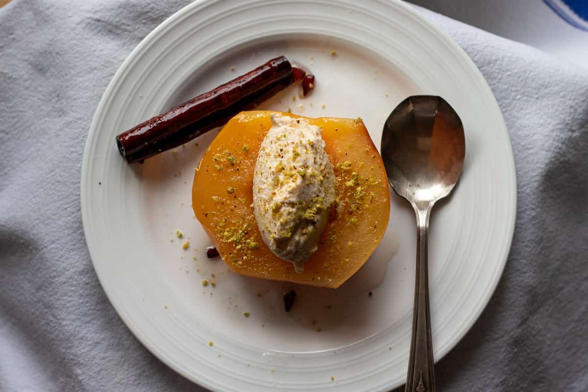 half piece of quince dessert is placed on a plate with clotted cream and a cinnamon stick