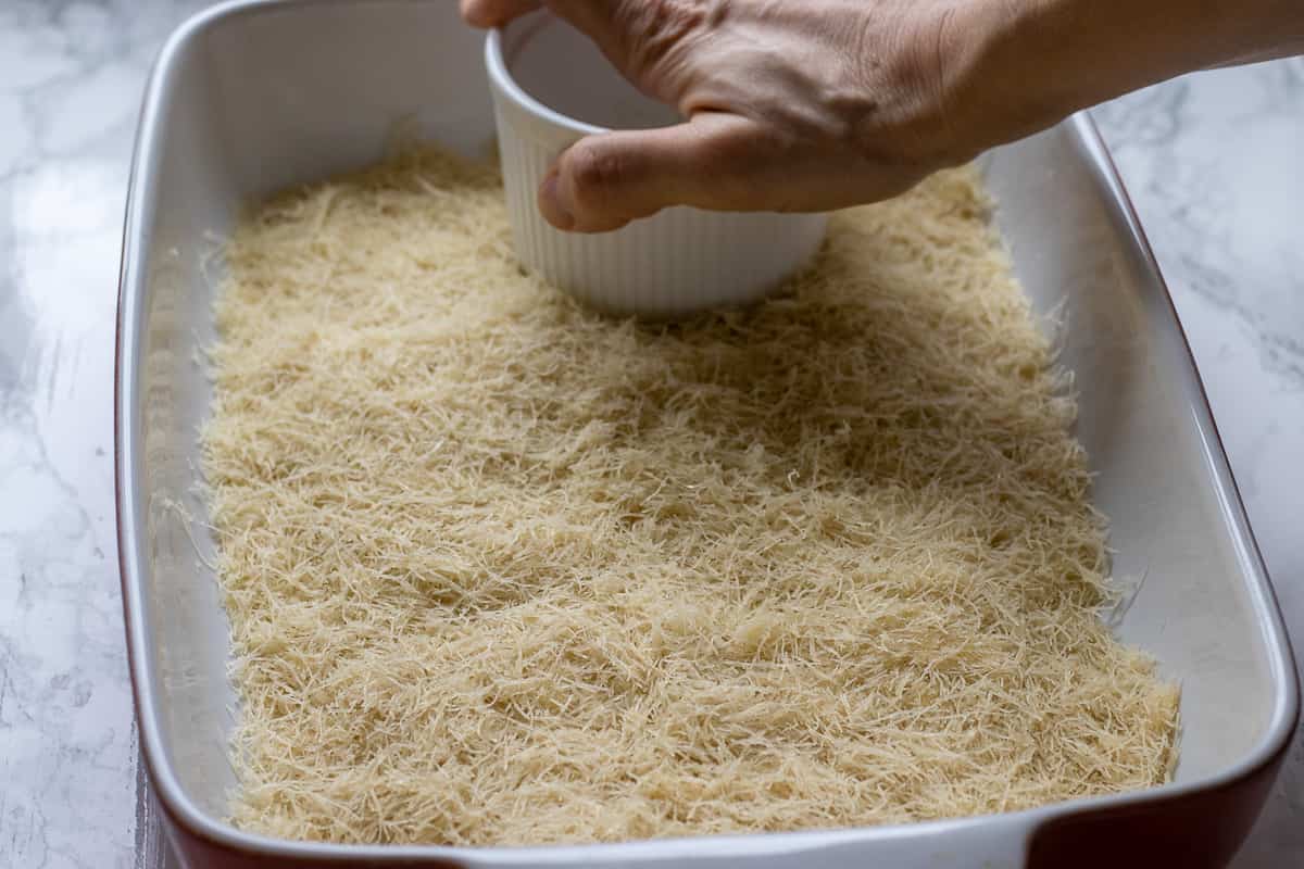 pressing down the kadaif into the bottom of a baking dish
