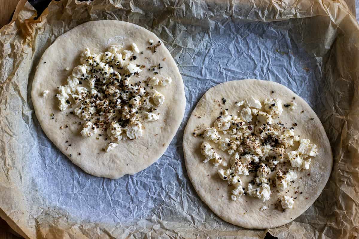 cheese and nigella seeds are spread over the dough circles