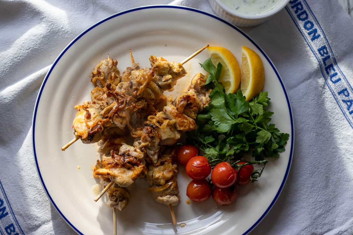joojeh kabab served with lemon slices, tomatoes, parsley and yogurt sauce on the side
