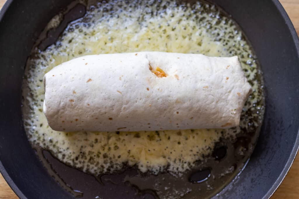 A rolled burrito is placed on top of the melted cheese.