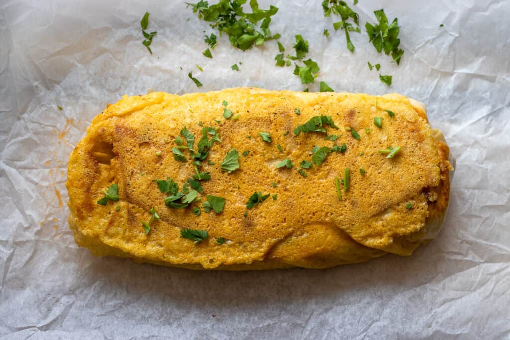 A piece of grilled cheese burrito garnished with chopped coriander.