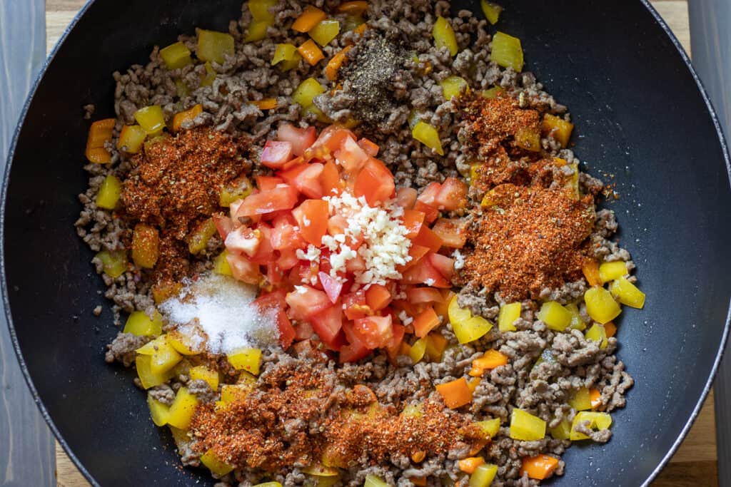 Chopped tomatoes, garlic, and taco seasoning are added to the pan.