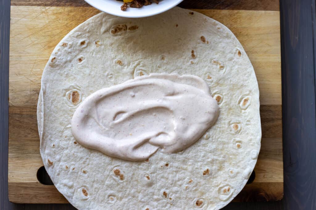 Sour cream and chipotle sauce is spread over a warm tortilla bread.