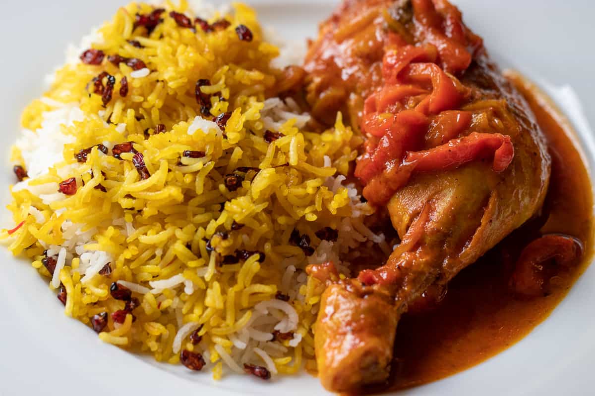a piece of chicken with vegetables served with saffron rice on a plate