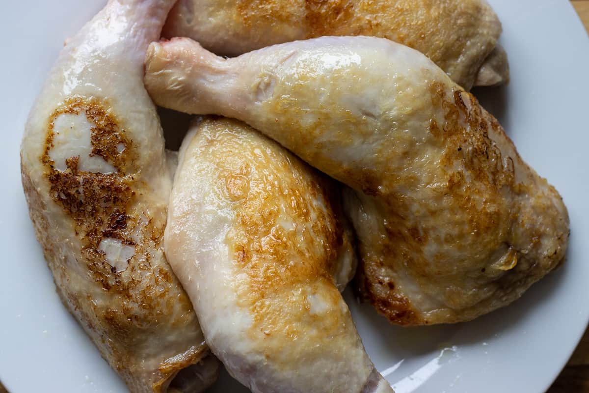 4 pieces of chicken legs are seared and set aside on a plate