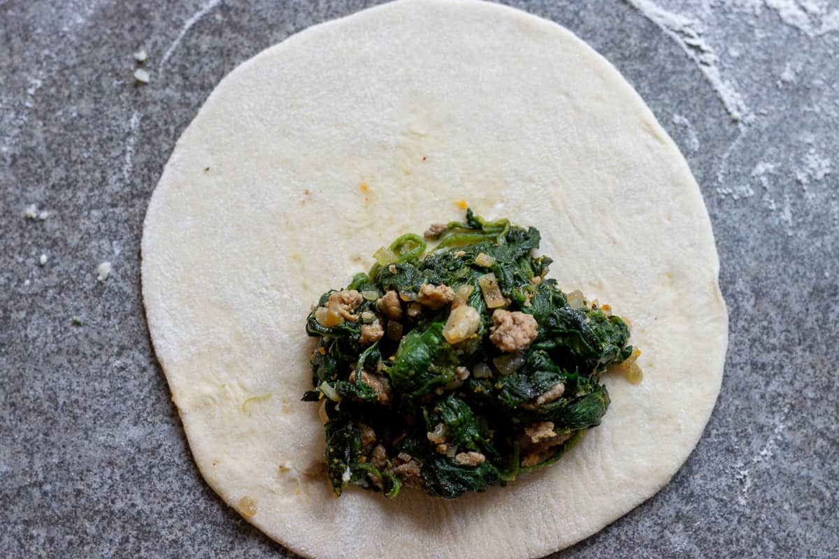 1.5 tablespoon of spinach filling is place on dough circle