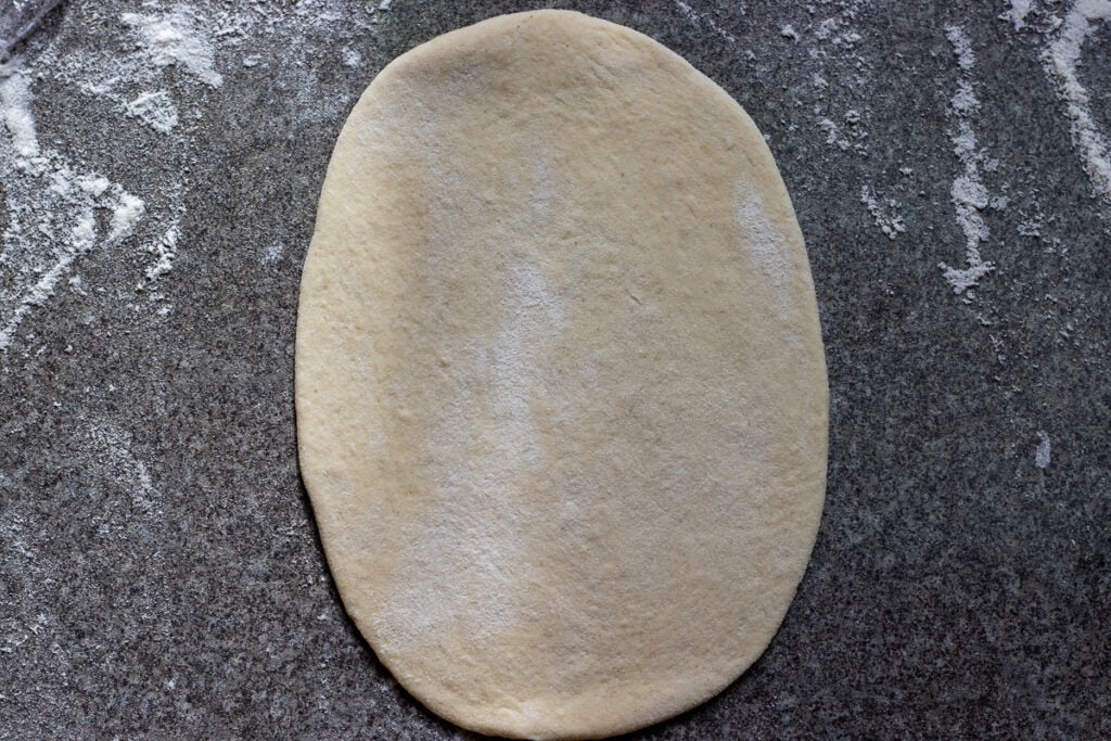 A dough ball is rolled out into an oval.