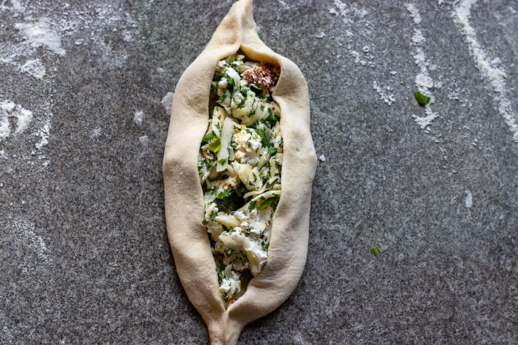 Sides of the dough are folded over the cheese filling to create a boat shape.