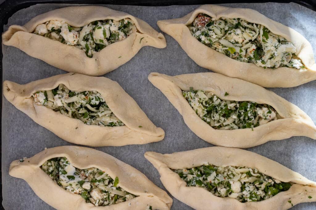 6 pieces of boat shaped cheese fatayer placed on a baking sheet.
