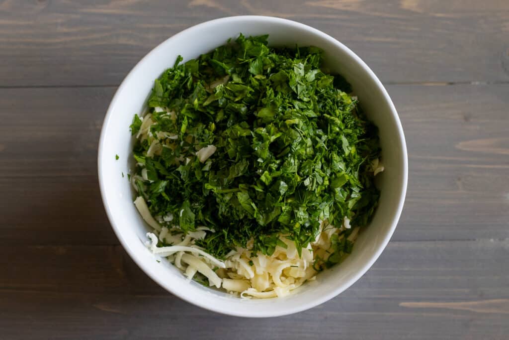 Cheese and herbs are placed in a bowl.