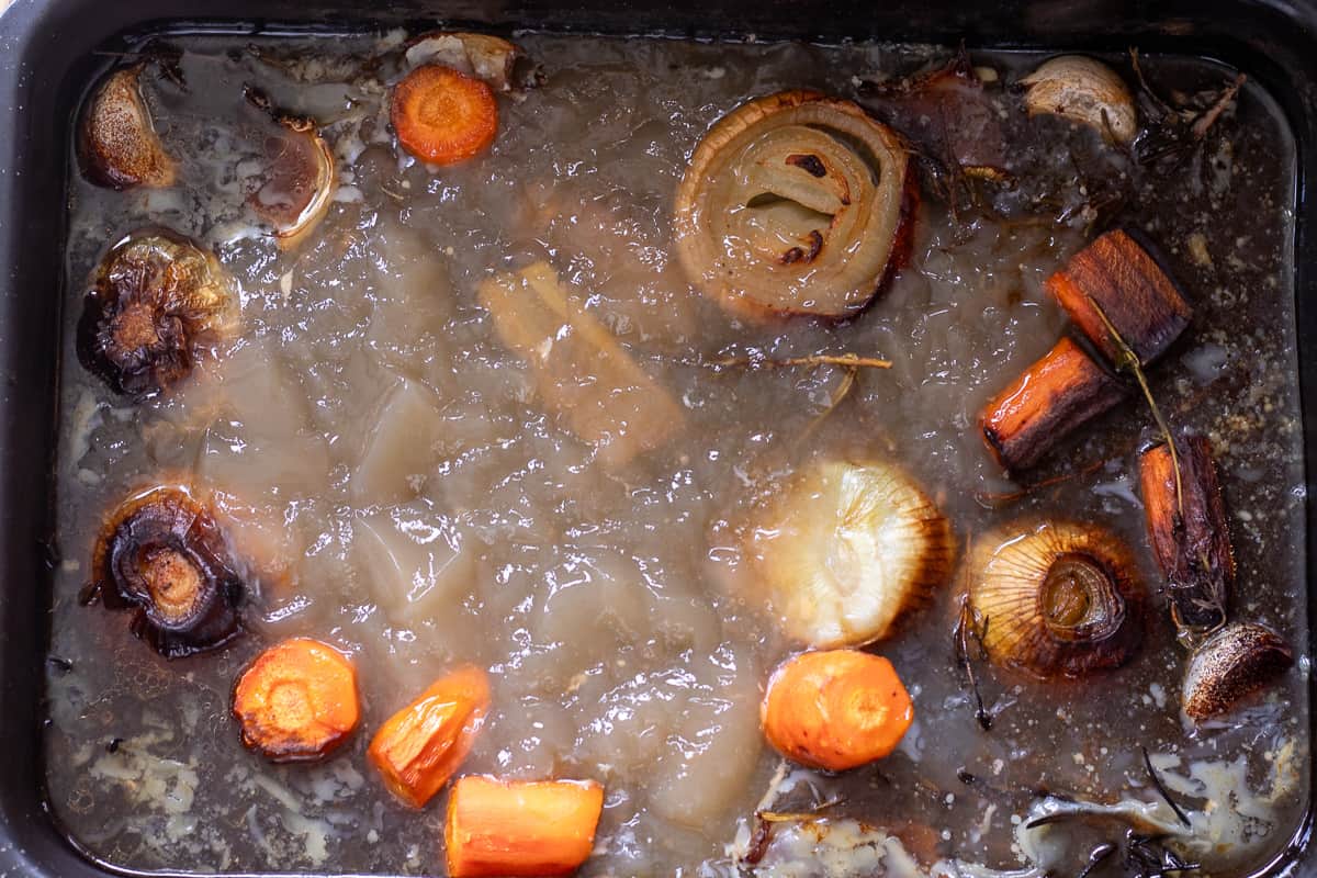 The stock and reduced marinade are placed on a baking tray with roasted vegetables to make the gravy.
