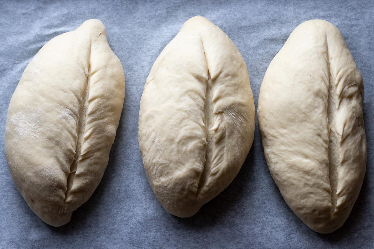Three bolillo breads have been slit lengthwise and are ready to bake.